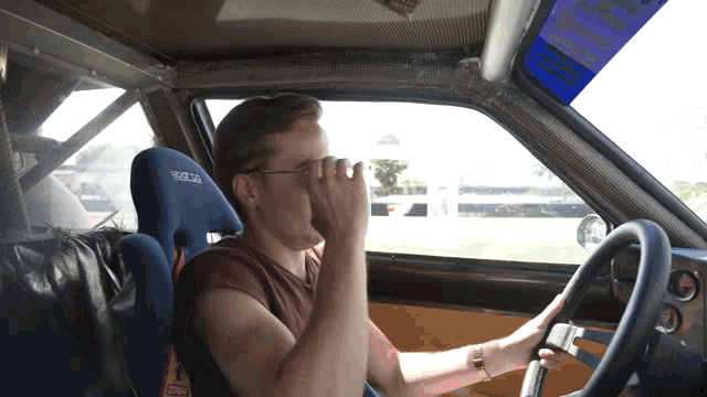 a man is sitting in a car with a blue sparco seat