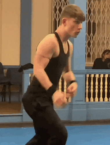 a man wearing a black tank top and black pants is standing on a blue mat