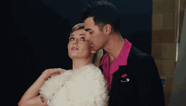 a man in a pink shirt kisses a woman on the forehead