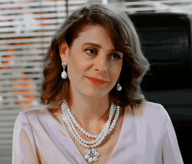 a woman wearing a pearl necklace and earrings smiles for the camera