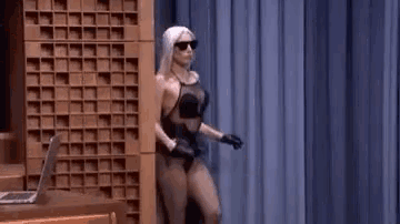 a woman in a black swimsuit is dancing on a stage in front of a blue curtain .