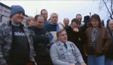 a group of men are standing around a man in a wheelchair who is wearing an adidas shirt