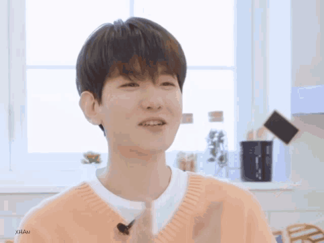 a young man wearing a pink sweater and a white t-shirt is smiling in front of a window .