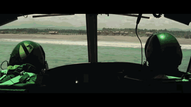 two pilots wearing green helmets are looking out of the cockpit of a plane