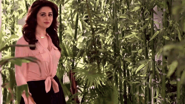 a woman in a pink top and black skirt is standing in a forest