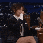 a woman in a suit is sitting in a chair with her legs crossed and covering her mouth with her hand .