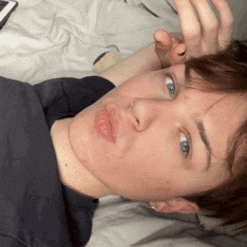 a young man laying on a bed with his hand on his head
