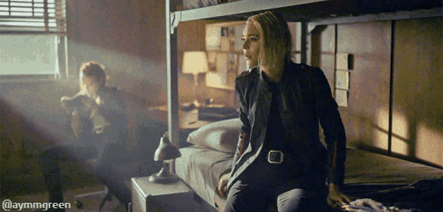 a woman is sitting on a bunk bed in a room with a man sitting on a chair .