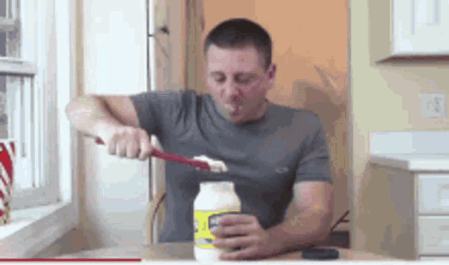 a man in a grey shirt is opening a jar of mayonnaise with a spatula
