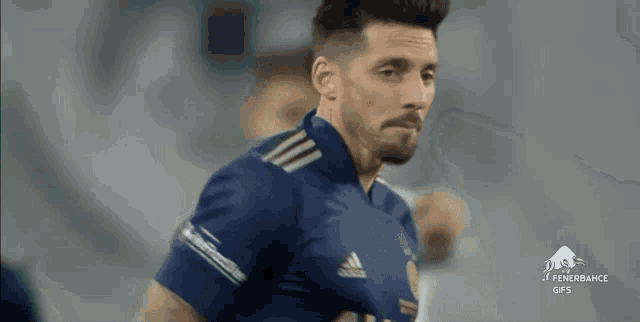 a soccer player in a blue adidas jersey is looking at the camera