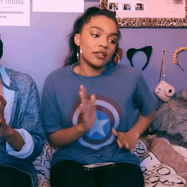 a girl wearing a captain america t-shirt sitting on a bed