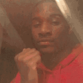 a man is smoking a cigarette in front of a mirror while wearing a red hoodie .