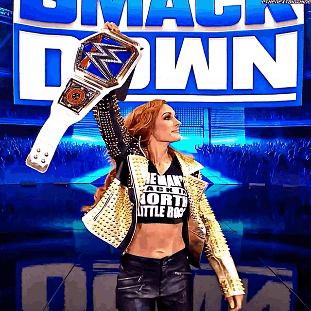 a woman holding a wrestling championship belt in front of a smack down sign