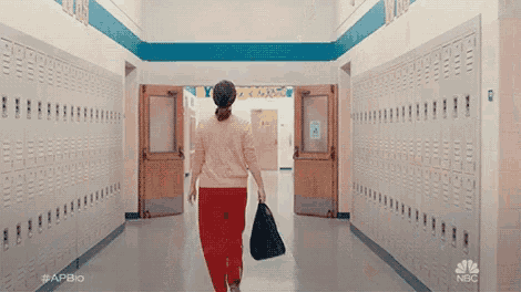 a woman is walking down a hallway with lockers and a bag .