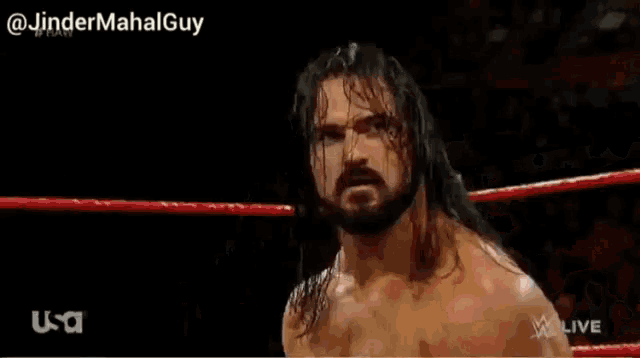 a man without a shirt is standing in a wrestling ring with red ropes .