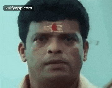 a man with a red symbol on his forehead is looking at the camera .