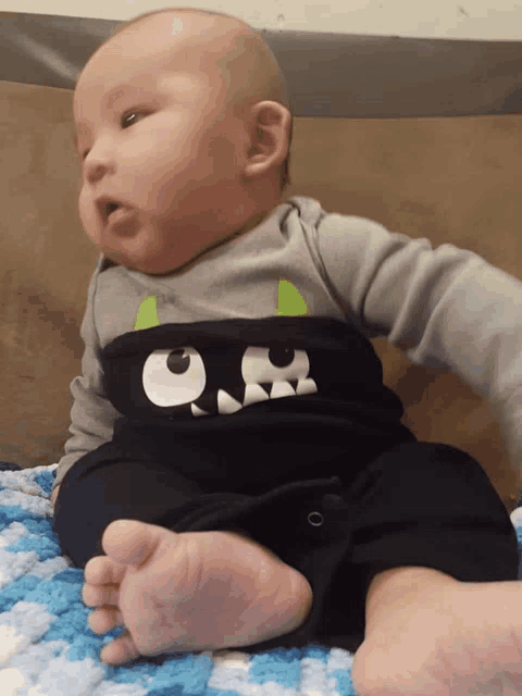 a baby wearing a monster shirt is laying on a blanket
