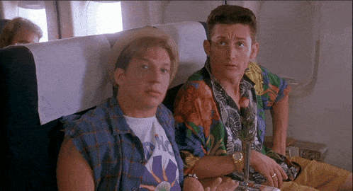 a man wearing a t-shirt that says nc sits next to another man on an airplane