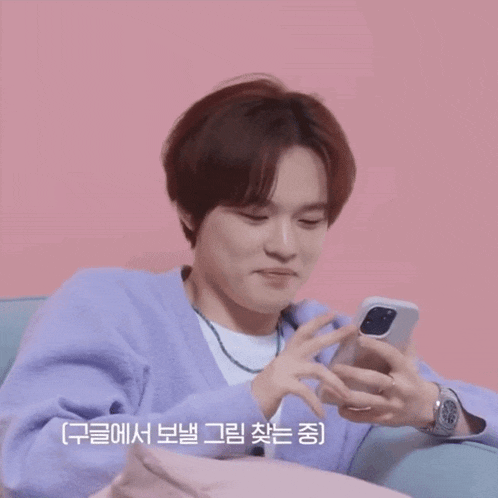 a man in a purple sweater is smiling while looking at his cell phone