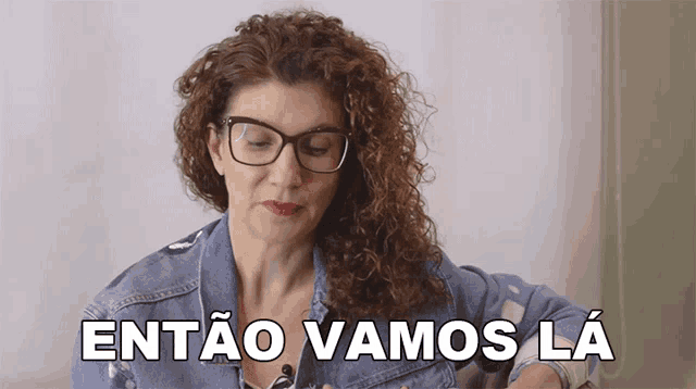 a woman with curly hair wearing glasses and a denim jacket says entao vamos la