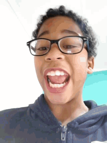 a young boy wearing glasses making a funny face with his tongue out
