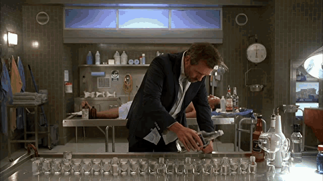 a man in a suit is standing in front of a table full of bottles and a clock