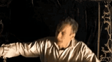 a man in a white shirt is standing in a dark room with his arms outstretched