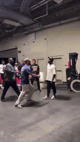 a group of men are dancing in a room with a forklift behind them