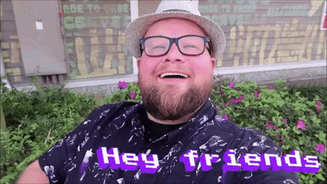 a man wearing glasses and a hat is smiling and says hey friends