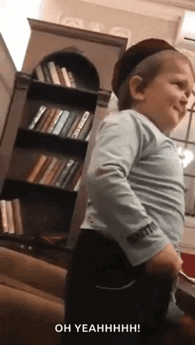 a little boy wearing a hat is standing in front of a bookshelf and says oh yeahhhh