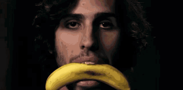 a man with a beard holds a banana in front of his mouth