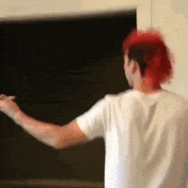 a man with red hair and a white shirt is standing in front of a black board .