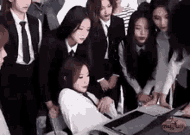 a group of people in suits and ties are standing around a woman sitting at a desk .