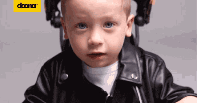 a young boy wearing a black leather jacket is sitting in front of a yellow sign that says doora