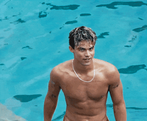a shirtless man wearing a necklace stands in front of a pool