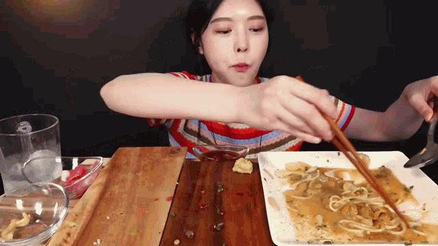 a woman is sitting at a table eating a plate of food with chopsticks
