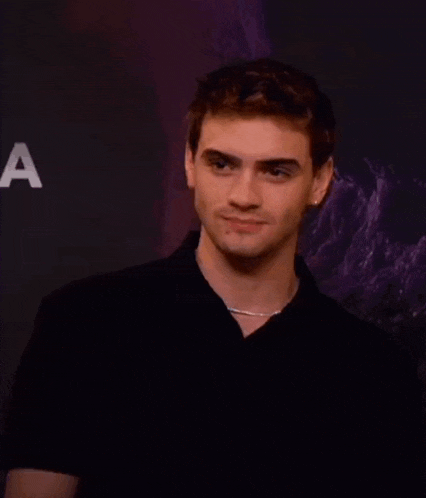a young man in a black shirt is standing in front of a purple wall and smiling .