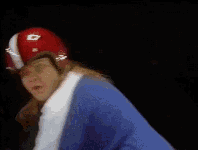 a man wearing a red and white helmet and a blue shirt is riding a skateboard .