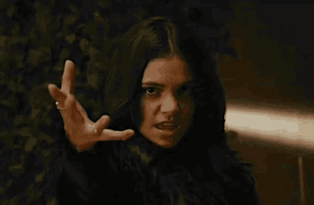 a woman with long black hair is making a funny face while holding her hand up .