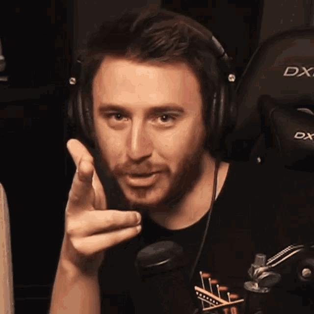 a man wearing headphones and a dx gaming chair is pointing at the camera