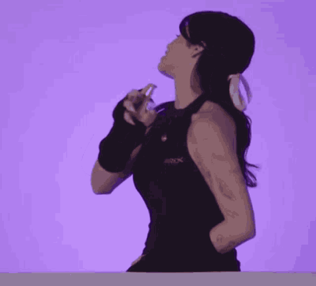 a woman in a black tank top is dancing in front of a purple background while holding a cell phone .