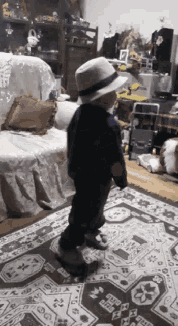 a little boy wearing a white hat is standing on a rug in a living room
