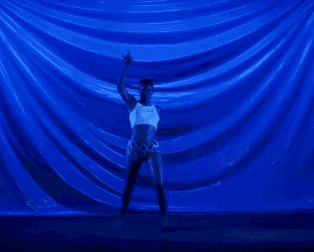 a man is dancing in front of a blue curtain .