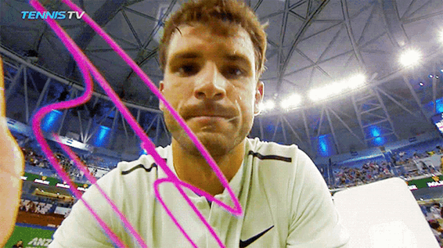 a man in a white shirt looks at the camera with a tennis tv logo behind him