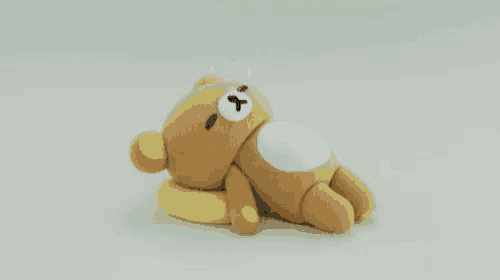 a rilakkuma teddy bear is laying on a yellow pillow on a white surface .