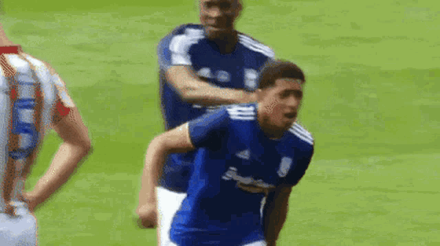 two men are playing soccer on a field and one of them is wearing a blue shirt with the letter b on it .