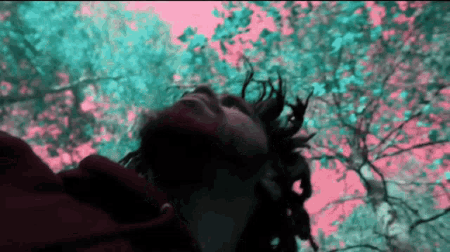 a man with dreadlocks is looking up at trees with a pink and blue background
