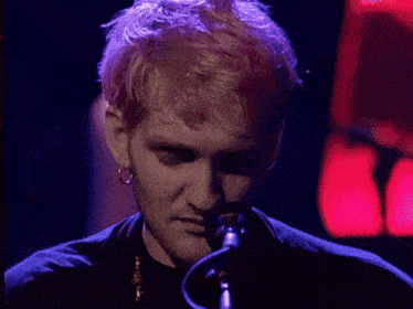a close up of a man singing into a microphone with purple hair