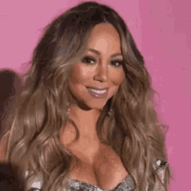 mariah carey is covering her face with her hand while standing in front of a pink wall .