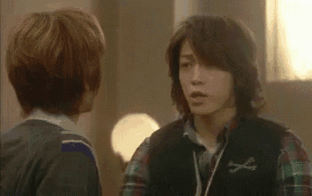 two young men are standing next to each other in a room . one of the men is wearing headphones .